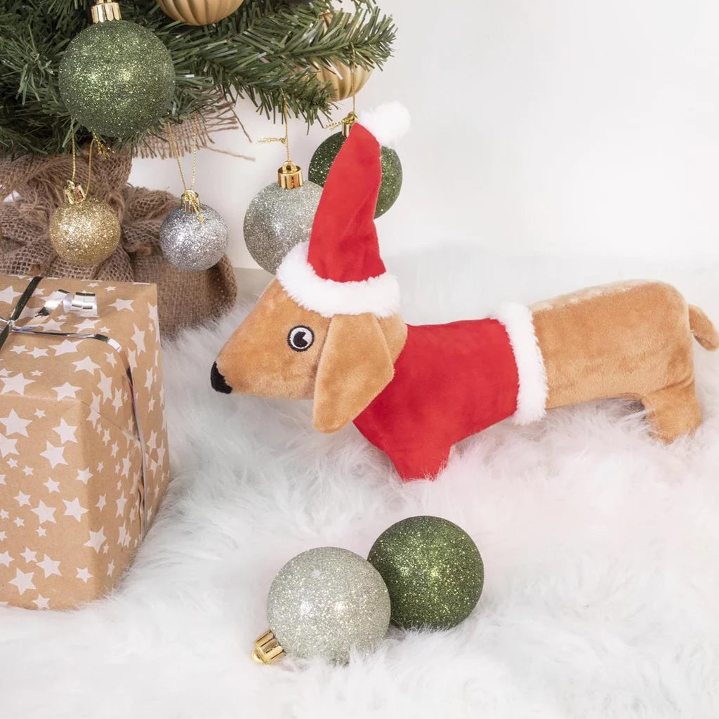 Santa Sausage Dog Toy under a Christmas tree among baubles and presents